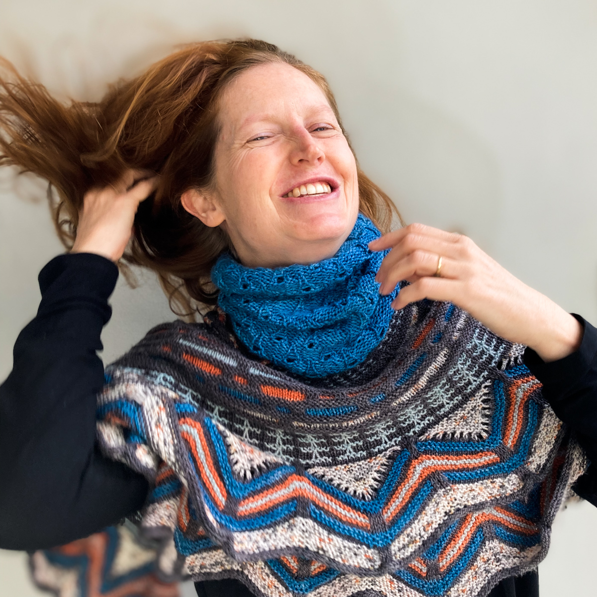 Bridget Henderson tosses her hair back wearing the Wild Weather Neckwarmer knit in Cowgirlblues Merino DK colour Guinea Fowl, and the Slipstravaganza Shawl knit in Cowgirlblues Merino Twist.