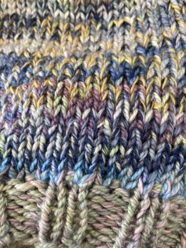 Close up of a knit showing how to change the colour with a combination of marled yarns and colours including pale green, light blue, indigo, purple and mustard