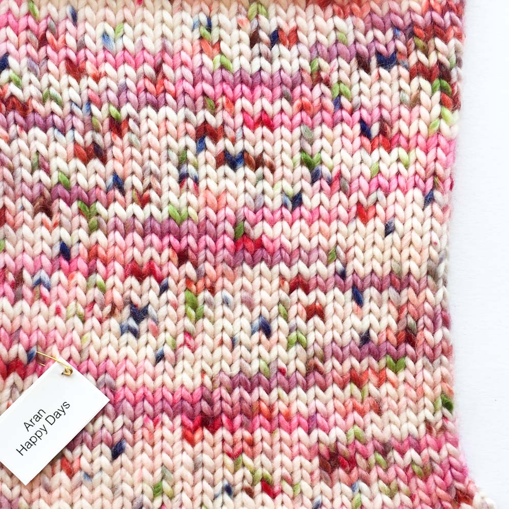 A knitted swatch in Cowgirlblues Happy Days colourway that includes shades of pink with pops of red, green and indigo blue