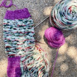 Stockinette hand knit sock in a busy variegated sock yarn colour Cowgirlblues Alanis Morisette with Girls Night purple cuff and heel